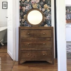 a dresser with a mirror on top of it in front of a floral wallpaper