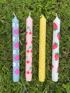 four candles are sitting in the grass with strawberries and cherries painted on them