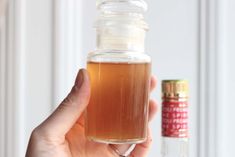 a person holding up a small glass jar filled with liquid next to an empty bottle