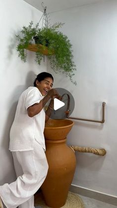 a woman standing next to a large vase with plants on the top and bottom of it