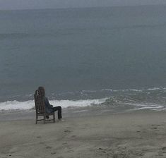 a person sitting in a chair on the beach next to the ocean and looking out at the water