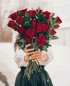 a woman holding a bunch of red roses in her hands while standing in the snow