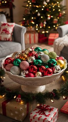 a white bowl filled with christmas ornaments on top of a table next to presents and trees