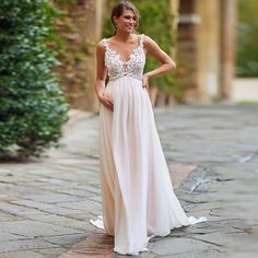 a woman in a long white dress standing on a brick walkway with her hands on her hips