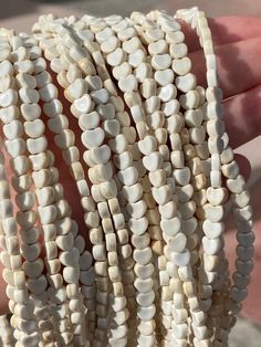 a close up of a person's hand holding several bracelets with white beads