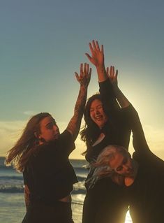 three women are standing on the beach with their arms in the air and one is holding her hands up