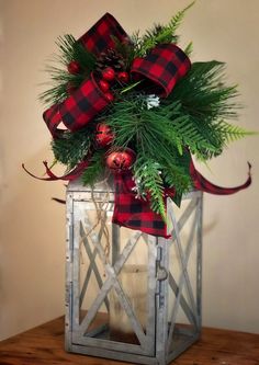 a christmas lantern with greenery and ornaments on it, sitting on a wooden table