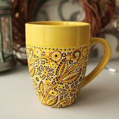 a yellow coffee cup with beaded designs on the outside and inside is sitting on a table