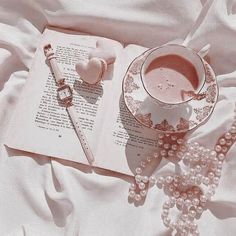 an open book with pearls and a watch on it next to a cup of coffee