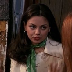 a woman with long hair wearing a white shirt and green scarf standing in front of a door