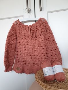 an orange sweater and ball of yarn are on a basket next to a white door