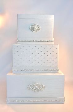 three tiered white wedding cake with crystal decorations on top and bottom layer, sitting in front of a light colored background