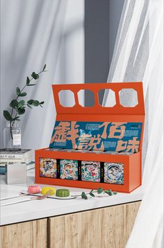 an orange box with four compartments on top of a table next to a plant and books