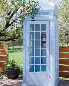 an old fashioned phone booth in the middle of a park with flowers growing out of it