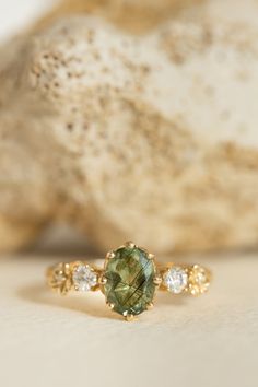 an oval green and white diamond ring sitting on top of a rock