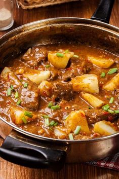 a pot filled with stew and potatoes on top of a wooden table next to a glass of water