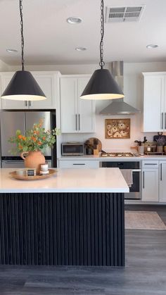 a large kitchen with white cabinets and black pendant lights over the island, along with potted plants