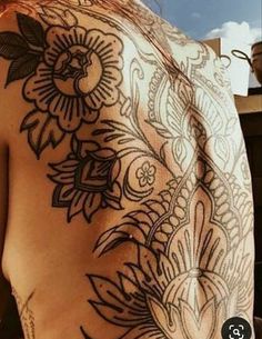 the back of a woman's shoulder with tattoos on it and flowers in the middle