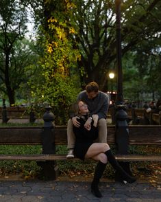 a man and woman sitting on a bench in the park at night with their arms around each other