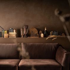 a brown couch sitting in front of a wooden shelf filled with books and vases