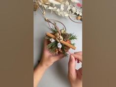 two hands are holding an ornament with pine cones and cinnamons