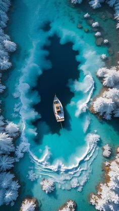 an aerial view of a boat in the middle of blue water surrounded by snow covered trees