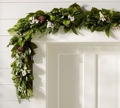 a white door decorated with greenery and flowers on the front of it, next to a wreath