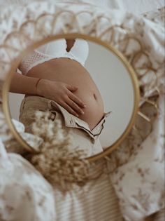 a pregnant woman's stomach is reflected in a round mirror on a bed with white sheets