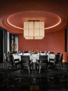 a round dining table with black chairs and white linens in a red walled room