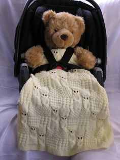 a teddy bear sitting in a stroller with a blanket on it's back