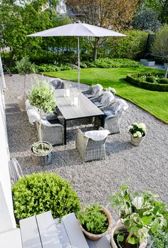 an outdoor dining table and chairs with umbrella in the middle of a graveled area