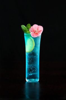 a blue glass with water and flowers in it on a black surface, against a dark background