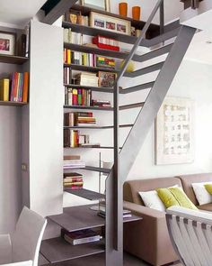 a living room filled with furniture and a metal stair case next to a table in front of a bookshelf