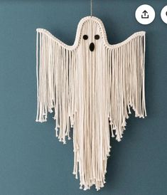 a white hanging decoration with fringes and eyes on it's face, in the shape of a ghost