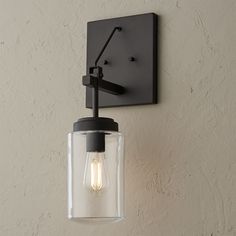 a light fixture mounted on the side of a wall with a clear glass jar hanging from it