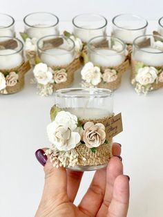 a hand holding a small glass jar with flowers on it and candles in the background