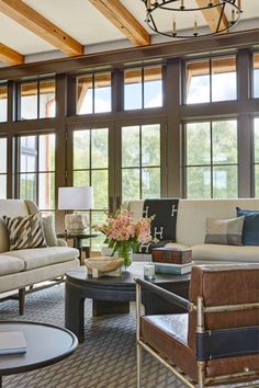 a living room filled with lots of furniture next to large windows on top of a wooden ceiling