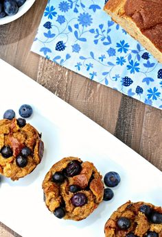 three blueberry muffins on a white plate next to two slices of bread