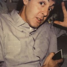 a man sitting in a chair making the peace sign with his hand while holding a cell phone