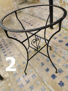 an iron table sitting on top of a tiled floor next to a black metal pole