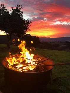 a fire pit sitting on top of a lush green field under a red sky at sunset