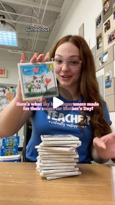 a woman holding up a video game in front of some stacks of books on a table