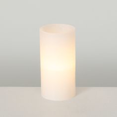 a white candle sitting on top of a table next to a gray wall and floor