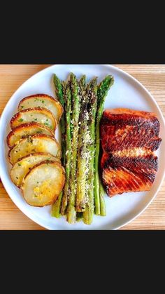 a white plate topped with asparagus, potatoes and meat on top of a wooden table