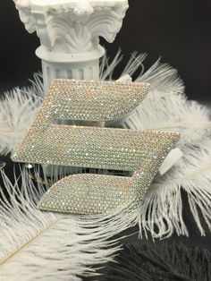 two pieces of jewelry sitting on top of a white feather covered table next to a vase