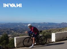 a man sitting on top of a bike next to a wall with mountains in the background