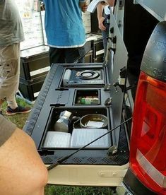 the back end of a car with its trunk open and two people standing around it