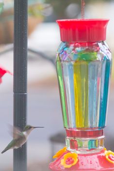 a hummingbird is flying near a colorful bird feeder with a hummingbird in the background