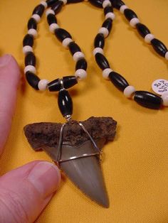 a person holding a piece of jewelry on a yellow table cloth next to a black and white beaded necklace