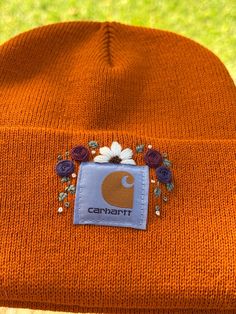 an orange beanie with flowers and the word canart embroidered on it's side